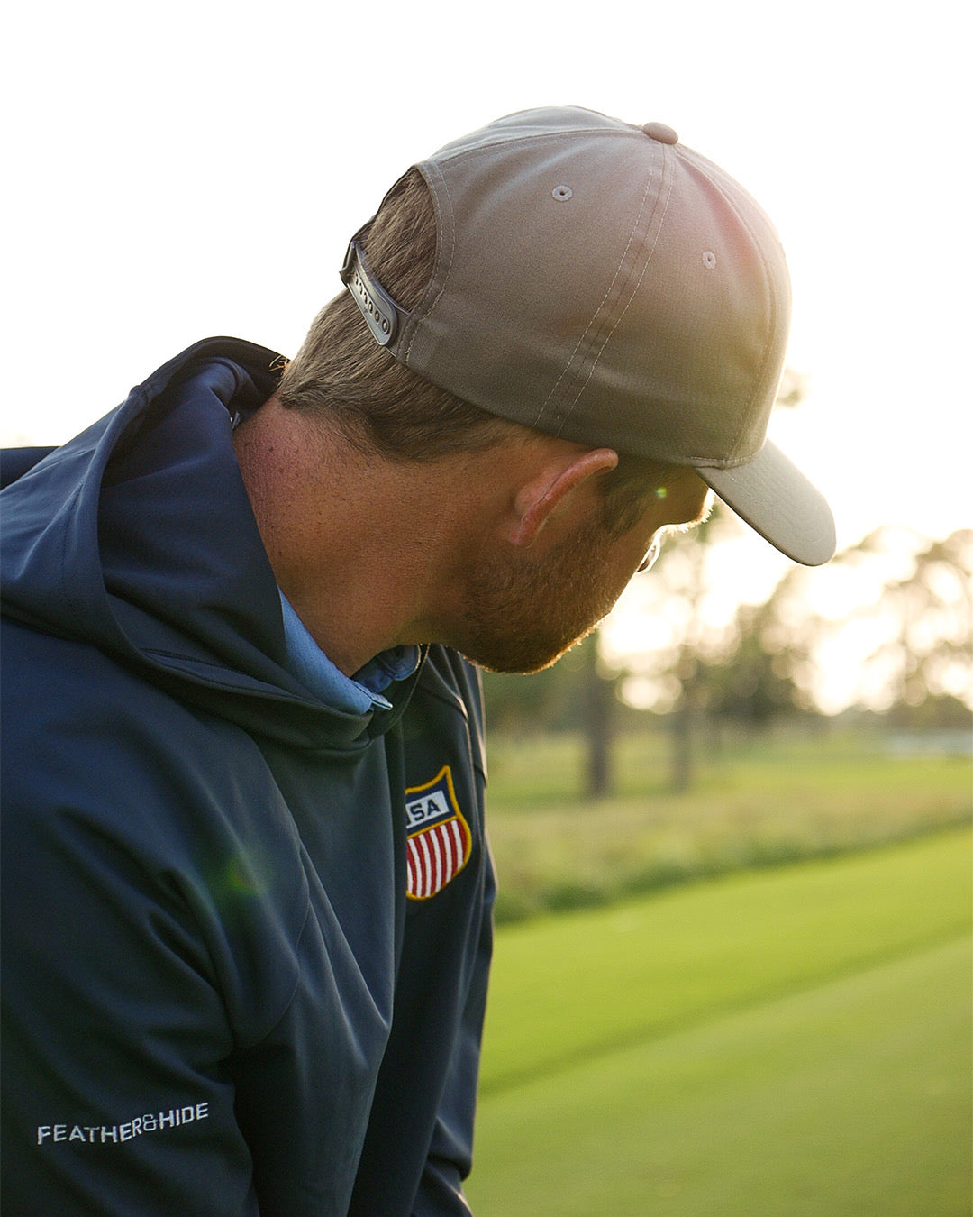Golfer wearing a cap and blue feather and hide hoodie with an American flag patch on a golf course