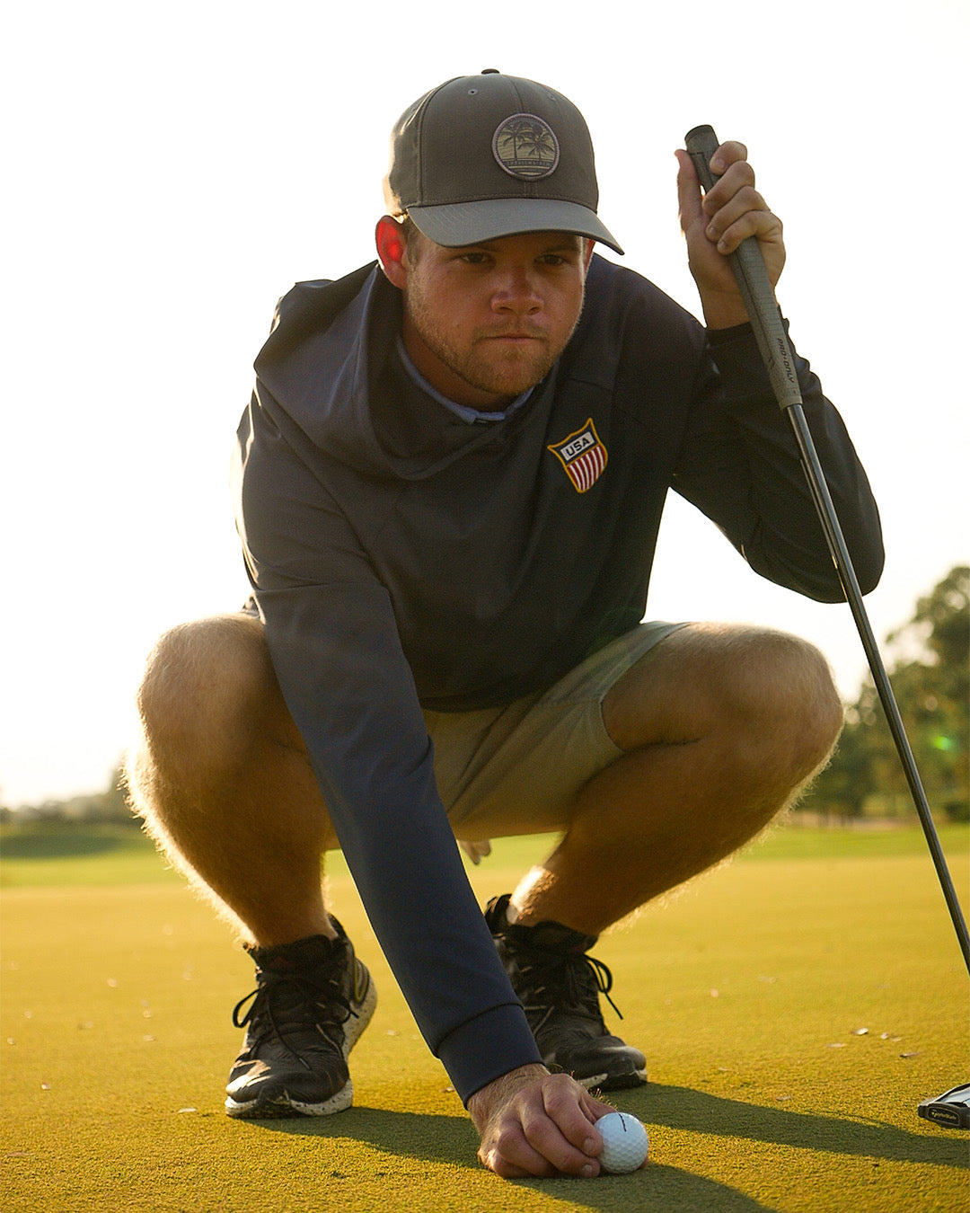 Golfer preparing to putt on a golf course with a Feather and Hide golf hoodie