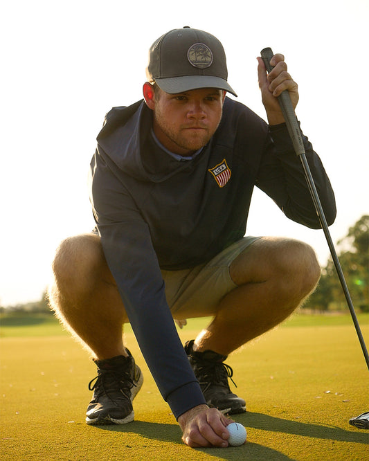 Golfer preparing to putt on a golf course with a Feather and Hide golf hoodie