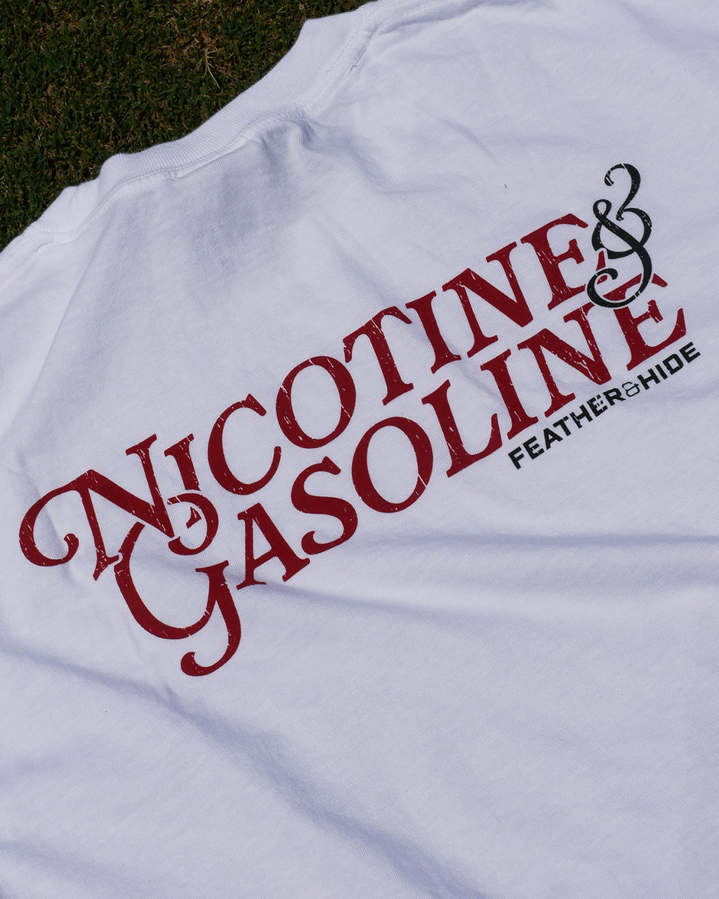 White t-shirt with red and black text 'Nicotine & Gasoline' on a grassy background