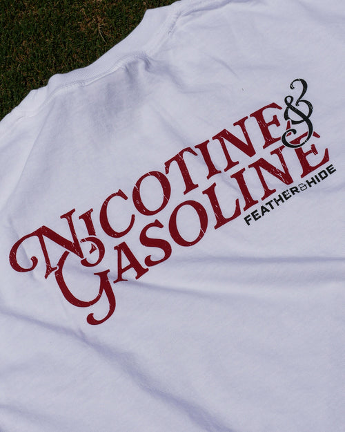 White t-shirt with red and black text 'Nicotine & Gasoline' on a grassy background