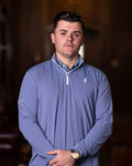 A man wearing a navy blue quarter-zip golf shirt with long sleeves, standing indoors.
