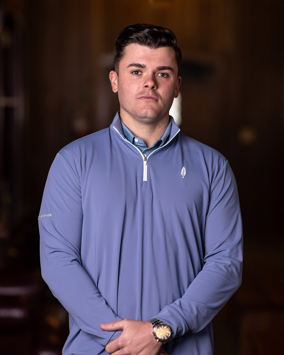 A man wearing a navy blue quarter-zip golf shirt with long sleeves, standing indoors.