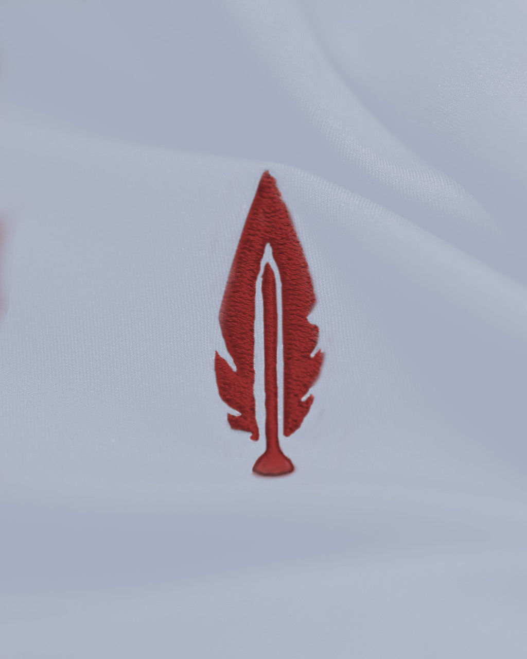 A small embroidered red feather patch on a white fabric background.