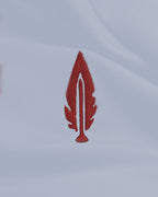 A small embroidered red feather patch on a white fabric background.