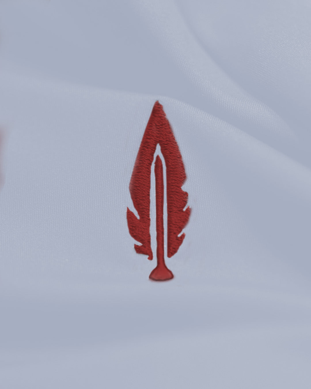 A small embroidered red feather patch on a white fabric background.