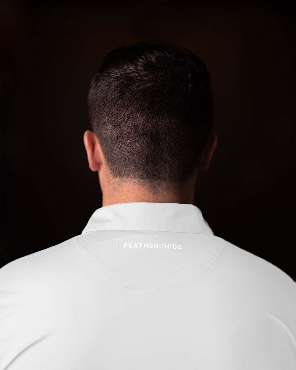 Man wearing a white shirt with 'FEATHER and HIDE' branding on a black background