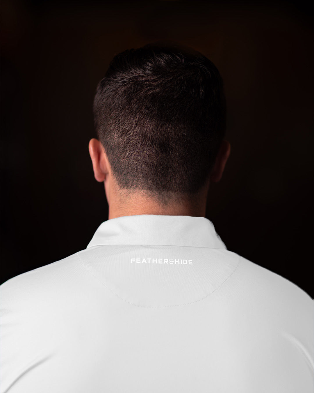 Man wearing a white shirt with 'FEATHER and HIDE' branding on a black background