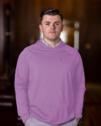 A man wearing a pale blue hoodie with a feather and hide golf logo on the chest, standing indoors.