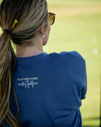 A woman viewed from behind wearing a navy blue t-shirt with 'FEATHERSHIDE and salty gaffer' printed in white on the back, set against a blurred green outdoor background.